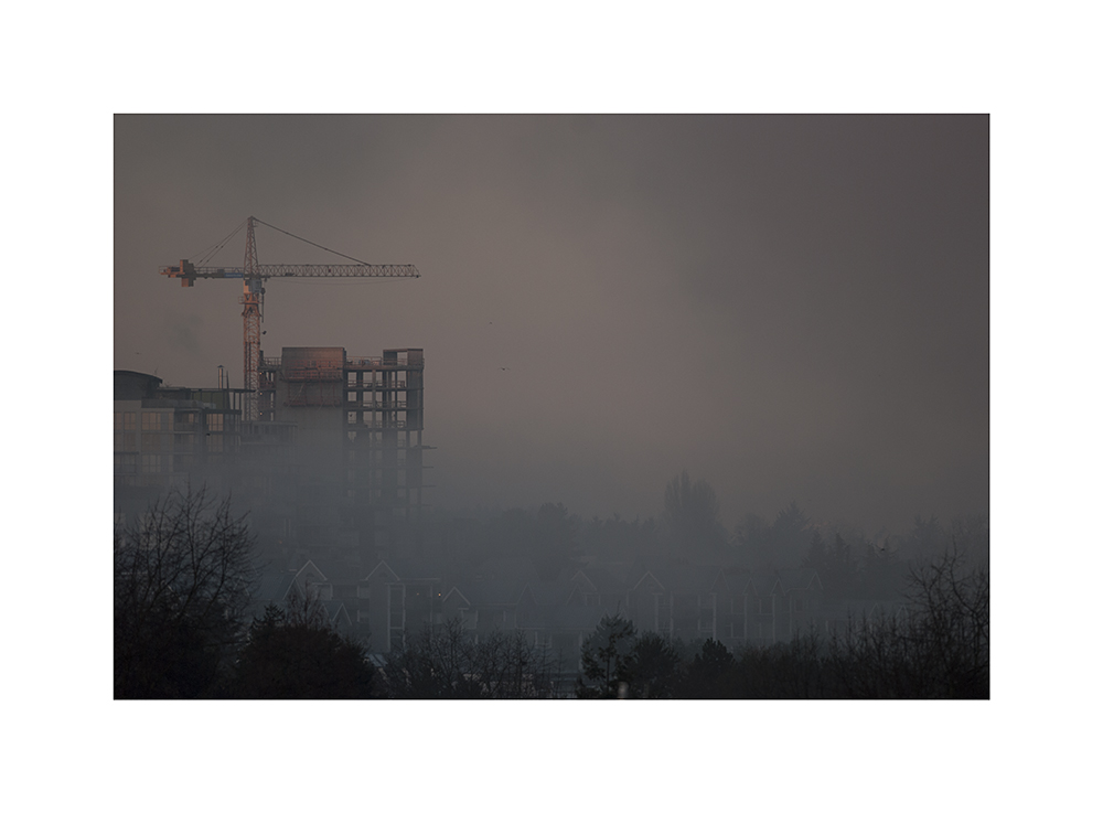 A crane rises above the fog.  That crane's been there for ages.  Will that building ever be finished?